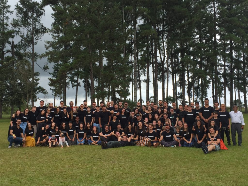 Large group of young people standing on grass facing camera with trees in the background