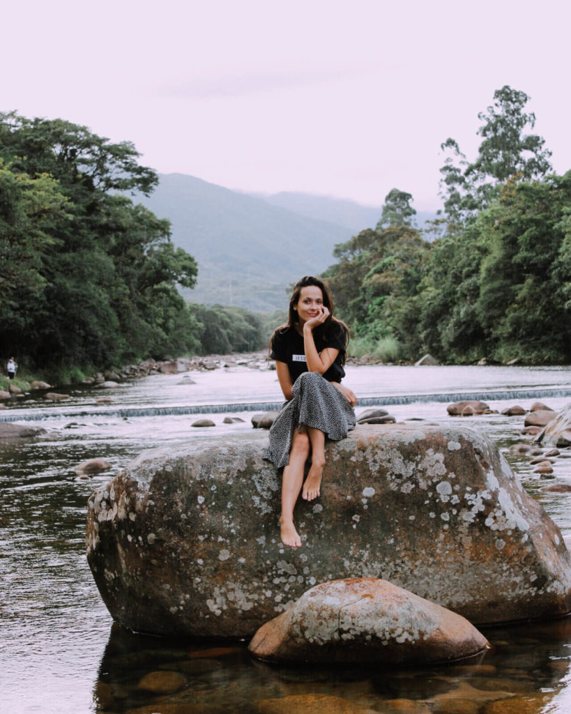 Girl sits on a large rock in middle of a river