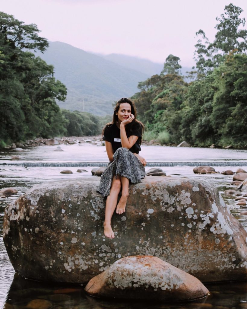 Girl sits on large rock in river