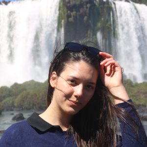 Young woman faces camera waterfalls in background
